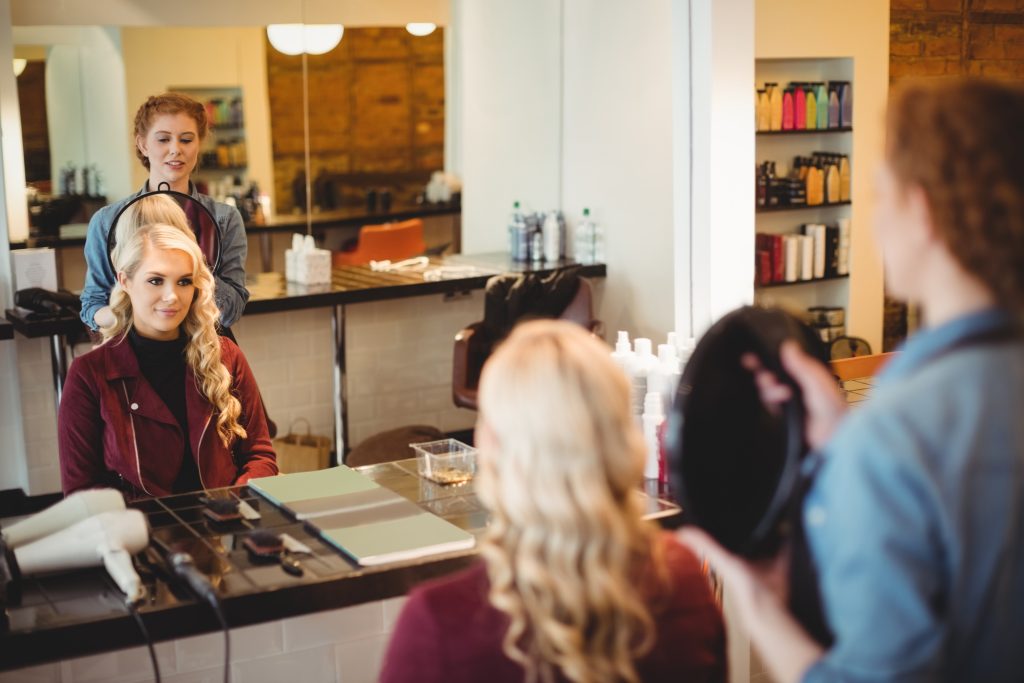 Female hairdresser styling clients hair in saloon