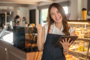 An Asian woman entrepreneur using tablet checking stock or sale income in modern coffee shop , concept small business